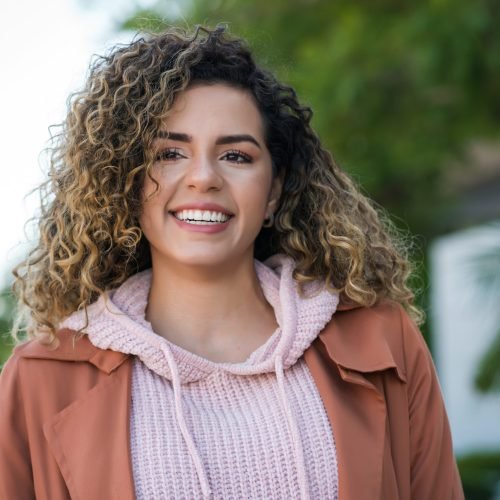 Young latin woman smiling while standing outdoors on the street. Urban concept.
